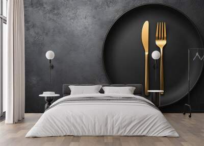 A black plate with a gold knife and fork on a dark grey background. Wall mural