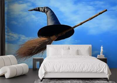 A black witch's hat sits atop a brown broomstick with a brown handle, against a backdrop of a bright blue sky with white clouds. Wall mural