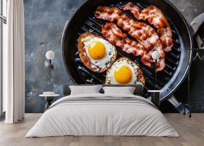 A close up shot of two fried eggs and crispy bacon in a black pan. The food is on a dark grey surface. Wall mural