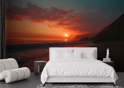 A stunning sunset over the ocean, casting an orange glow on the water and beach.  The sun is setting behind a line of mountains, with a large rock in the foreground. Wall mural