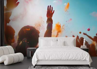 A woman with her arms raised in the air, covered in orange and purple powder, as a large group of people throws colorful powder into the air.  The sky is bright blue, and the sun is shining. Wall mural