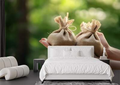 Two small burlap sacks are held by a hand, with a blurry green background. Wall mural