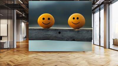 Two yellow smiley faces painted on round objects are sitting on a wooden beam. Wall mural