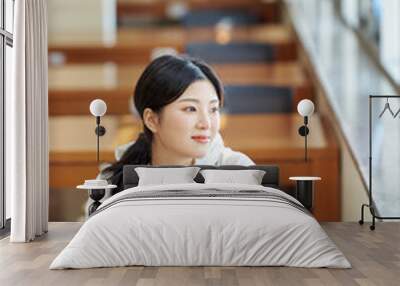 Asian Korean University Library Young female college student model sitting at a desk by a window with light coming in, reading a book, looking out the window Wall mural