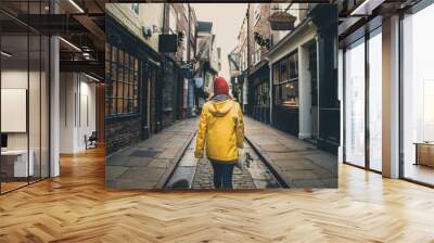 A rear view of a girl in a yellow coat walking along the historic street known as The Shambles in York, UK which is a popular tourist destination and medieval landmark in this ancient city Wall mural