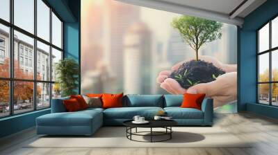 Hand holding young plant against blurred urban background. eco friendly earth day concept. Wall mural