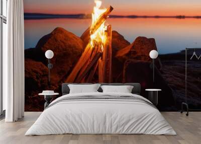 Fire and flames of atmospheric campfire on the beach at night. Still water of the lake on the backgound with warm colors of sunset.    Wall mural