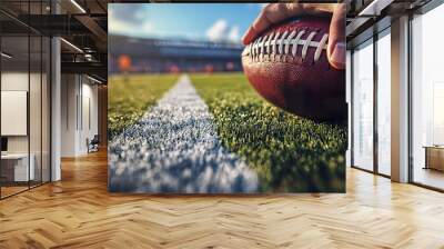 Close up of hand holding American football on vibrant green field, ready for game. Wall mural