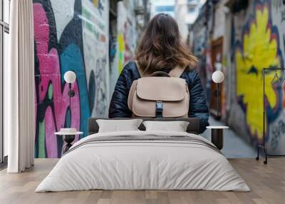 Person walking in an urban alleyway with colorful street art and a backpack. Wall mural