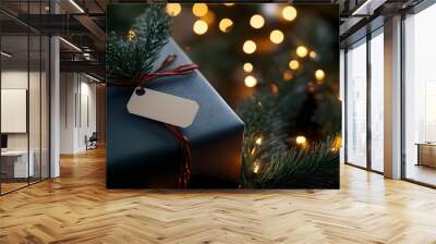 A beautifully wrapped Christmas gift with a blank tag, nestled among festive lights and greenery, perfect for holiday celebrations. Wall mural