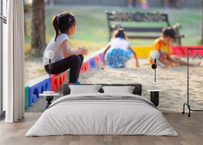 Little child girl sitting lonely watching friends play at the playground.The feeling was overlooked by other people. Wall mural