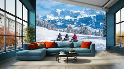 Snowmobiles travel through a scenic winter landscape with snowy mountains and trees under a clear blue sky. Wall mural