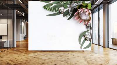 Beautiful pink King protea surrounded by Australian native eucalyptus leaves and gum nuts, creating a floral border, photographed from above, on a white background. Wall mural