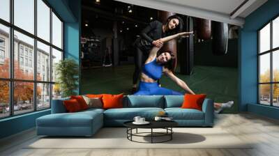 Two beautiful young girls doing fitness in a gym. Stretching the muscles of the legs and arms. Wall mural