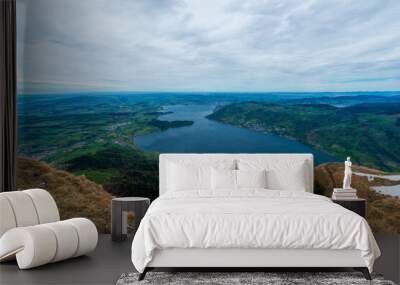 A Swiss Alps vista reveals a stunning panoramic view of Lake Lucerne nestled amidst rolling green hills, framed by a dramatic sky with swirling clouds. Wall mural