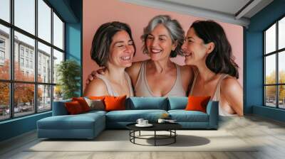 Three women with short hair laughing together against a pink background, celebrating friendship and joy in a casual indoor setting Wall mural