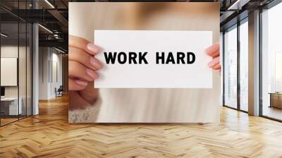 Close-up of hands holding a white card with the text 'WORK HARD'. Represents motivation, dedication, and hard work in achieving goals. Wall mural