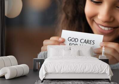 Smiling girl holding a card with a motivational message reading 'God Cares for You', sharing positive vibes and encouragement. Wall mural