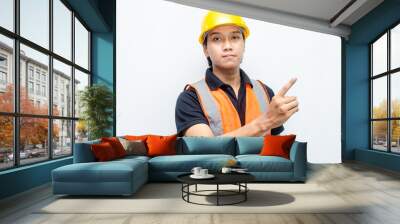 asian man consrtruction worker wearing yellow safety helmet and orange vest smiling and pointing finger to copy space with happy and surprised expression. Wall mural