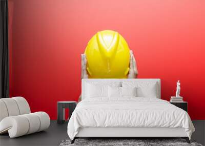 Male hand holding yellow safey hard hat isolated over red background. work safety concept. labour day concept. Wall mural