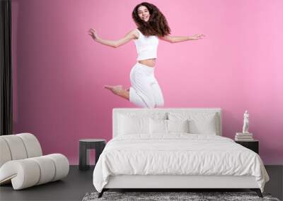 Happy girl jumping for joy, mid-air pose, sporty, active and energetic, pink background Wall mural