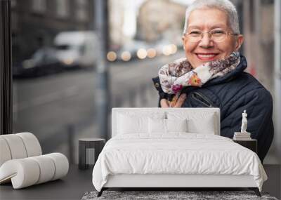 Portrait of beautiful senior woman with a jacket on a windy day in an urban city environment, happy and cheerful Wall mural