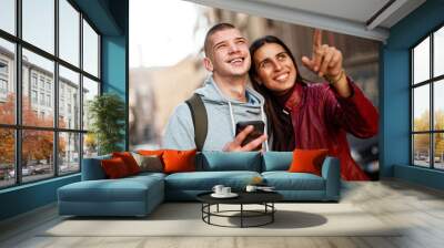 Young teenage couple visiting a foreign city, looking at the landmarks around them, navigating with their phone Wall mural