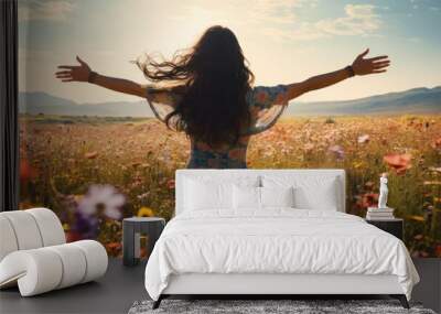 A black haired woman stands in a field of flowers and spreads her arms, rearview, mountains, spring, summer Wall mural