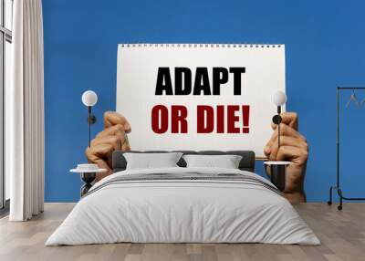 Adapt or die text on notebook paper held by 2 hands with isolated blue sky background. This message can be used as business concept about adaptation. Wall mural