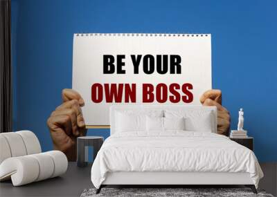 Be your own boss text on notebook paper held by 2 hands with isolated blue sky background. This message can be used as business concept to encourage audience to take control of your life. Wall mural