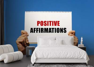 Positive affirmations text on notebook paper held by 2 hands with isolated blue sky background. This message can be used as business concept about positive affirmation. Wall mural