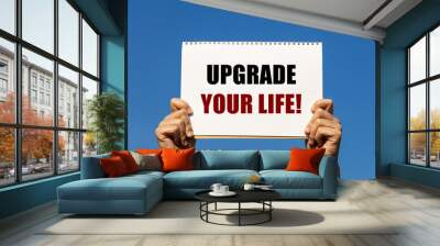 upgrade your life text on notebook paper held by 2 hands with isolated blue sky background. this mes Wall mural