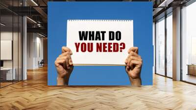 What do you need question text on notebook paper held by 2 hands with isolated blue sky background. This message can be used as business concept about what do you need. Wall mural