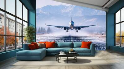 A large aircraft takes off from a snowy runway surrounded by majestic mountains in the early morning light Wall mural