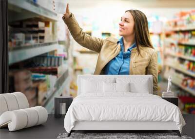 Female customer holding package or item in supermarket. Woman taking product from shelf in grocery store. Retail, sale and consumerism concept. Happy lady buying groceries. Wall mural