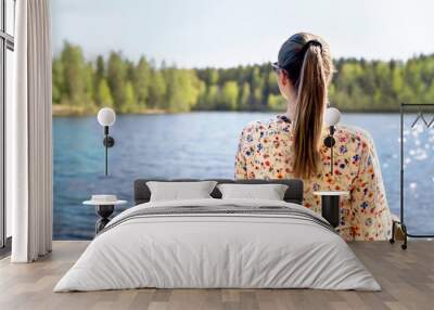 Finnish woman standing and looking at a lake in Finland. Happy person relaxing and enjoying sunny summer vacation or weekend in nature. Back view of carefree lady in dress. Wide banner. Wall mural