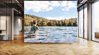 Lake in Finland. Woman swimming. Finnish nature, water and serene sky in summer. Outdoor bathing in Scandinavia after sauna. Green forest and beach in the morning or day. Lakeside back view portrait Wall mural