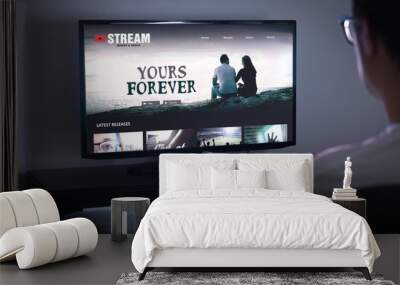 Online movie stream service in smart tv. Streaming series with on demand video (VOD) service in television. Man choosing film to watch with remote. Person sitting on couch at home late at night. Wall mural