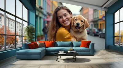 A joyful woman smiles as she holds a playful golden retriever puppy in a colorful alleyway during the golden hour Wall mural