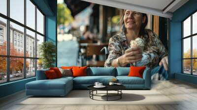 A woman in a wheelchair is sitting outside with an ice cream cone in her hand Wall mural