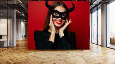 A woman wearing a black mask and hat strikes a playful pose against a vibrant red backdrop during a festive celebration Wall mural