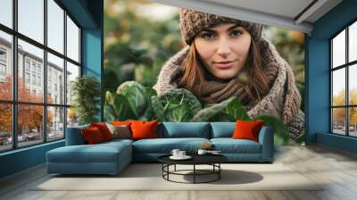 A woman wearing a brown hat and scarf is standing in a field of green plants Wall mural