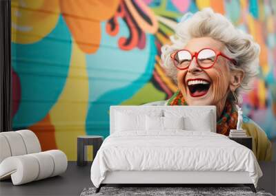 Very bright and happy old woman laughing in stylish glasses on a multi-colored background Wall mural