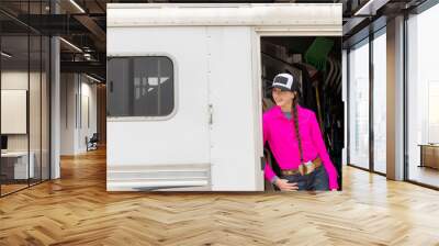 Barrel racer Cowgirl in bright pink shirt and hat in horse trailer Wall mural