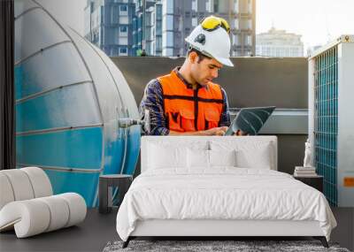 Male technical foreman inspects maintenance working in laptop with to look at plumbing and electrical systems on the roof of a building, maintenance in sewer pipes area at construction site. Wall mural