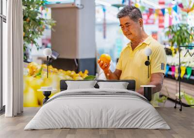 Old senior asian man looking at tangerine while enjoying grocery shopping at in the supermarket Wall mural