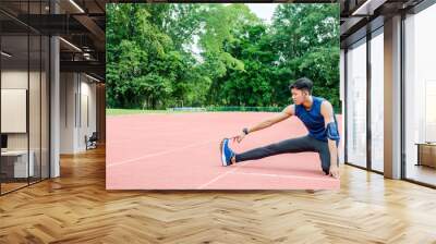 One male athletes is warming-up, One runners sitting on the racetrack at the stadium stretching their legs before running Wall mural