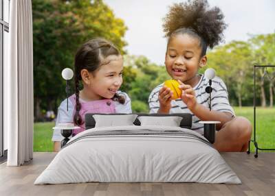 Two African American little girl sitting on the mat and eating oranges fruits in the autumn park , play with oranges fruits Wall mural