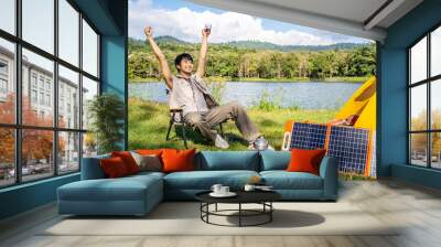 Young Asian traveling man relax and enjoy outdoor lifestyle camping in forest mountain on summer holiday. Attractive male drinking coffee and raise your hands refreshingly in the midst of nature Wall mural