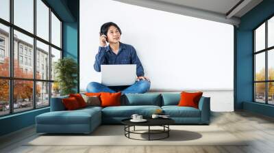 Young man asian sitting on the floor with using computer laptop smiling and listening nice music and feel relieved from stressed posing isolated over white wall, copy space.. Wall mural